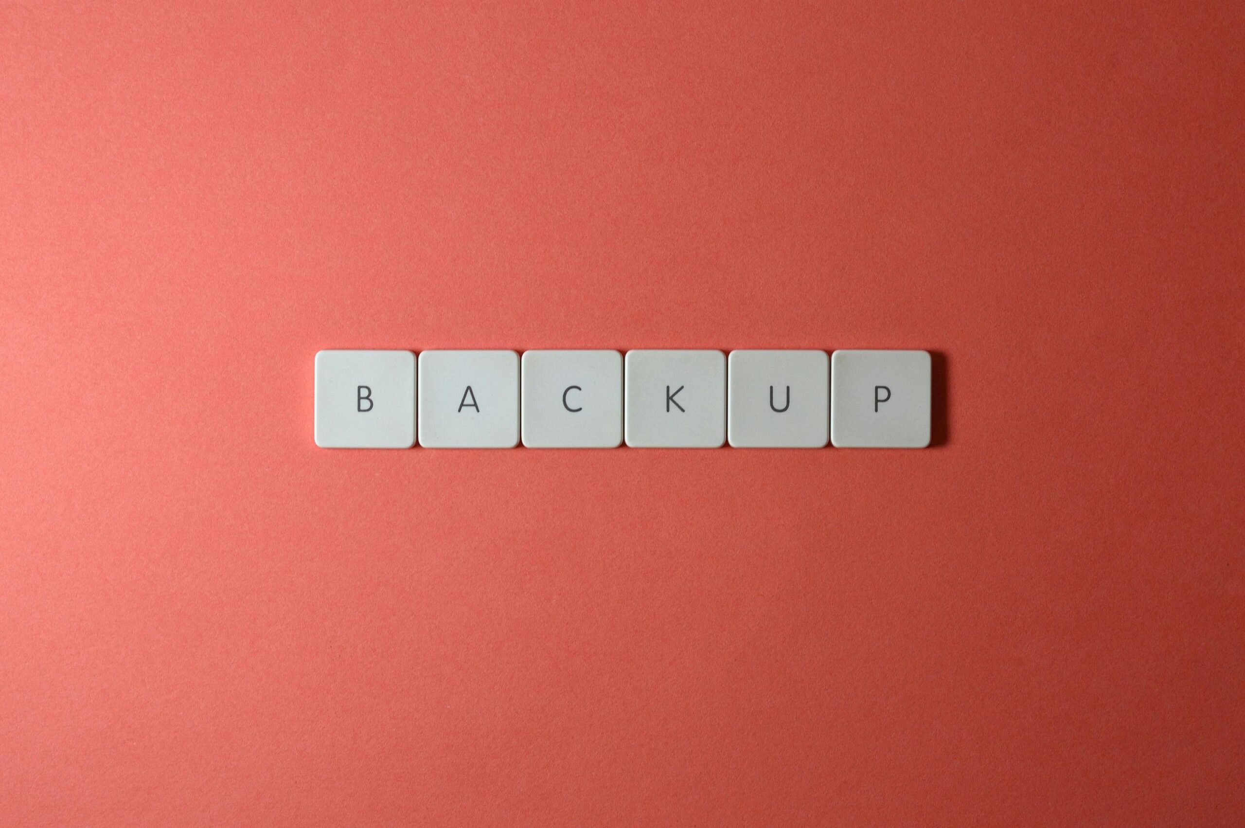 Simple-Backup-and-Recovery-Plans-Every-Small-Business-Needs-scaled.jpg Free Close-up of keyboard keys spelling 'BACKUP' placed on a coral-colored surface. Stock Photo